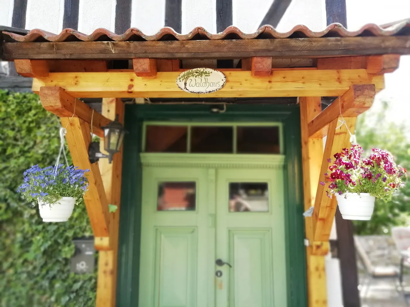 Grüne Doppeltür des Hauses mit Holzvordach und Blumenampeln